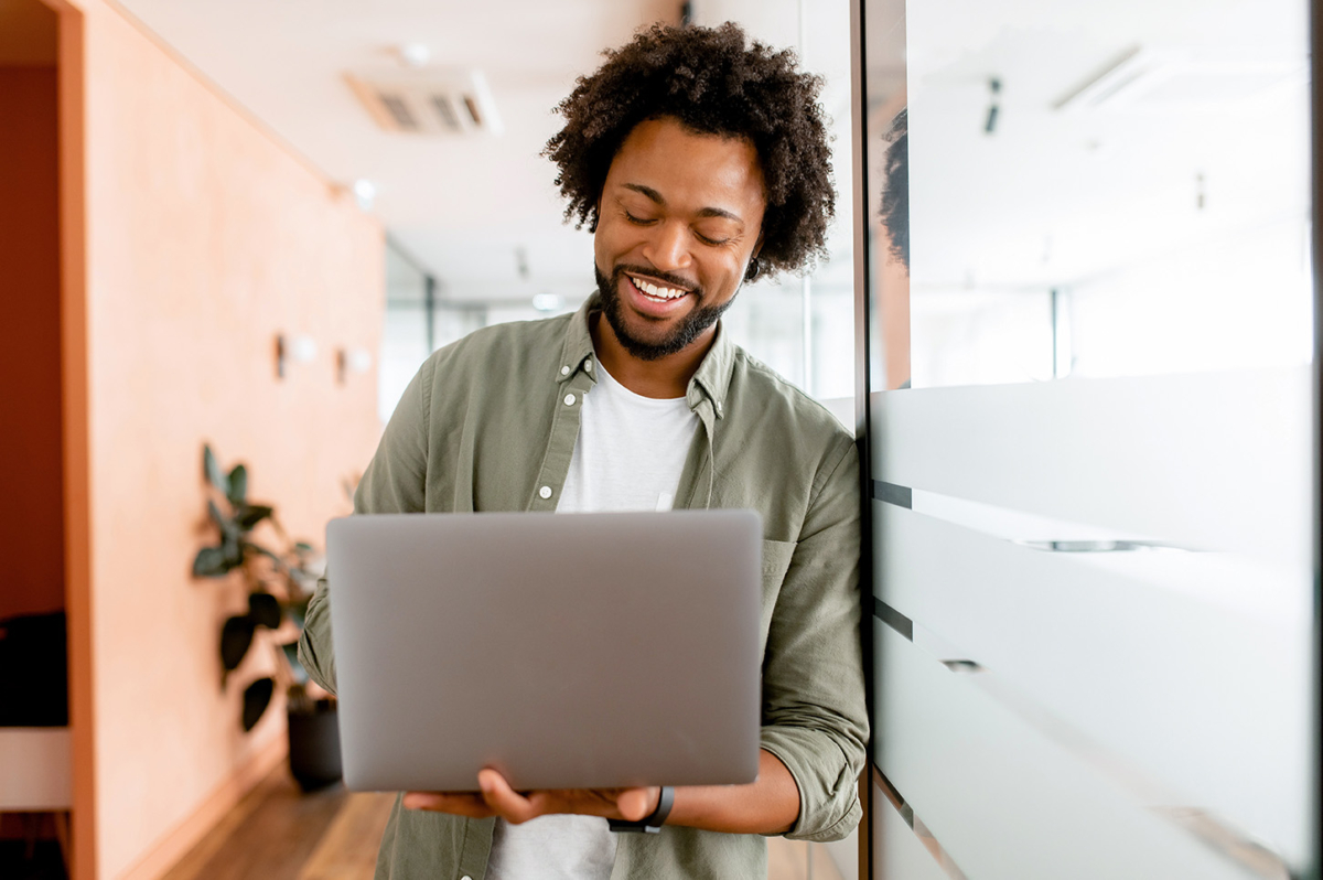 Young african-american businessman standing in office hallway with his laptop.