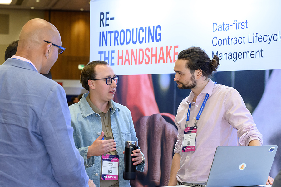 three men at an Agiloft booth standing in front of a sign that says re introducing the handshake