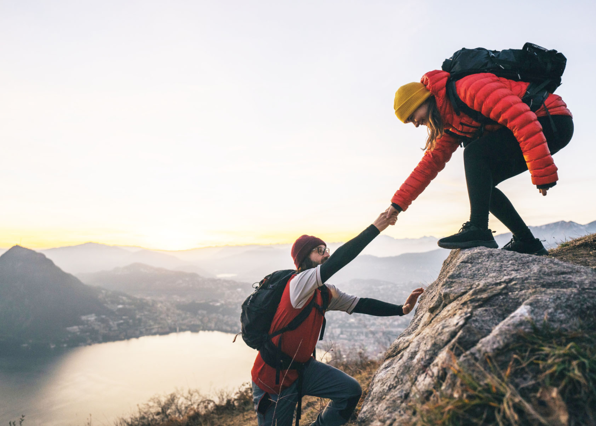 a person helping another person climb a mountain