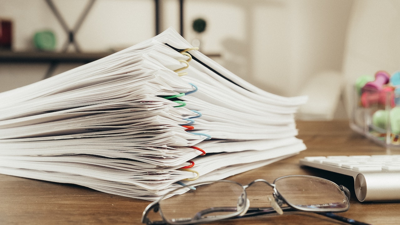 Stack of papers and glasses on top of a wooden table.